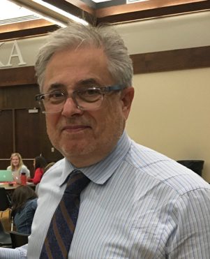 A man with glasses and a tie in front of other people.