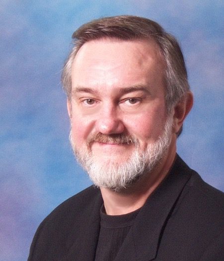 A man with grey hair and beard wearing black.